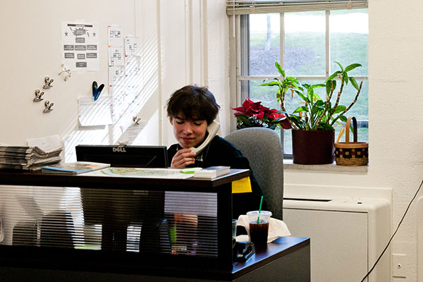 A student sitting behind a desk answering the phone.