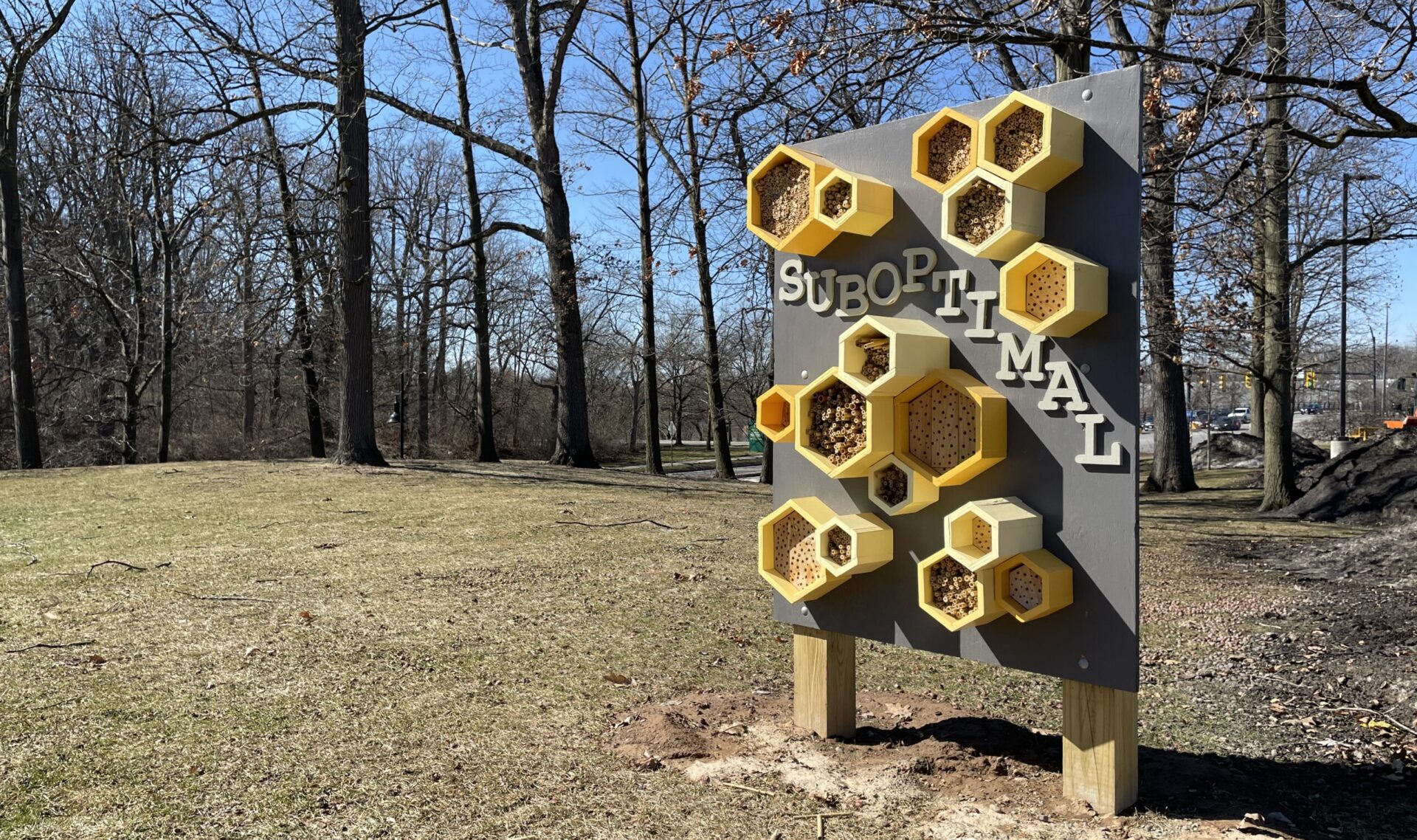 Solitary bee nesting structure on a display in a field. The bee domicile has several hexagonal nesting places and is accompanied by the word 