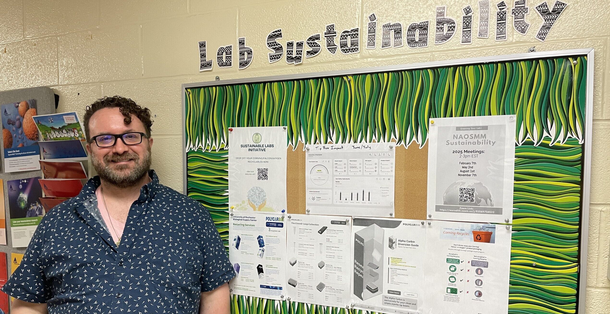 Man standing in front of 'Lab Sustainability' corkboard with posters about sustainable lab practices.