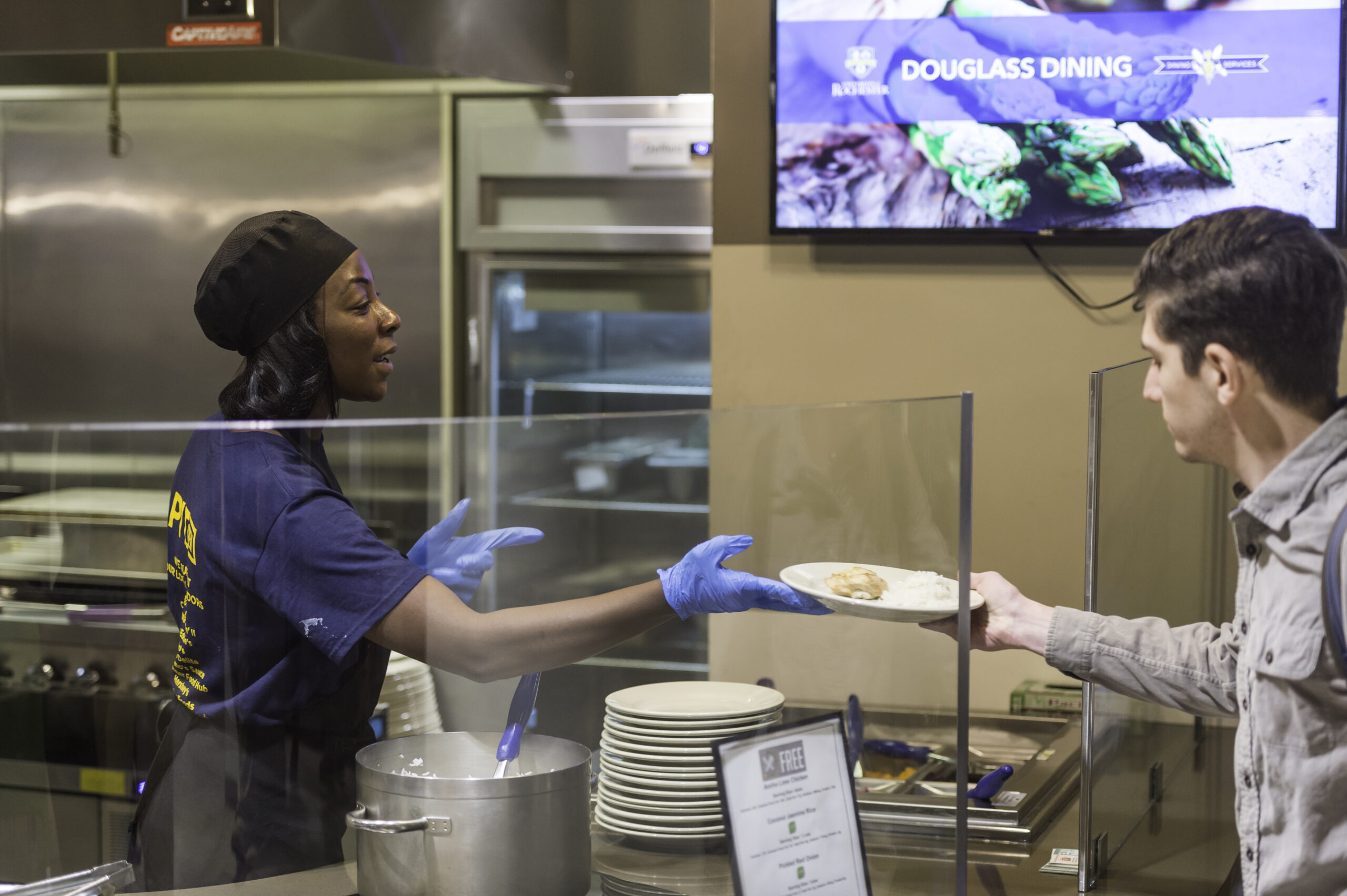 Woman handing plate of food to student in dining hall