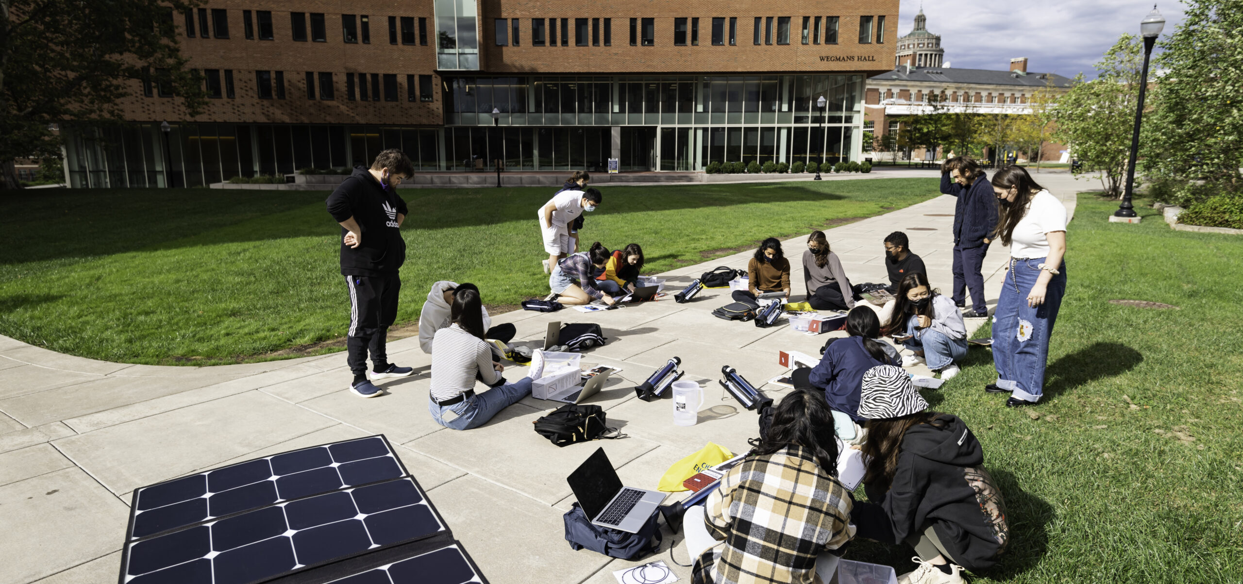 Students in class studying solar panels outside on sunny day