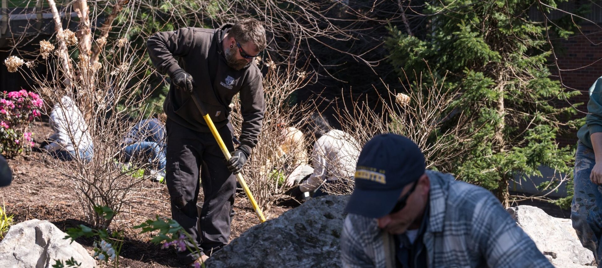 Man digging with shovel in garden on sunny day.
