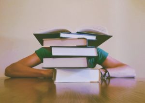 Student resting their head and sleeping behind a stack of books on a desk