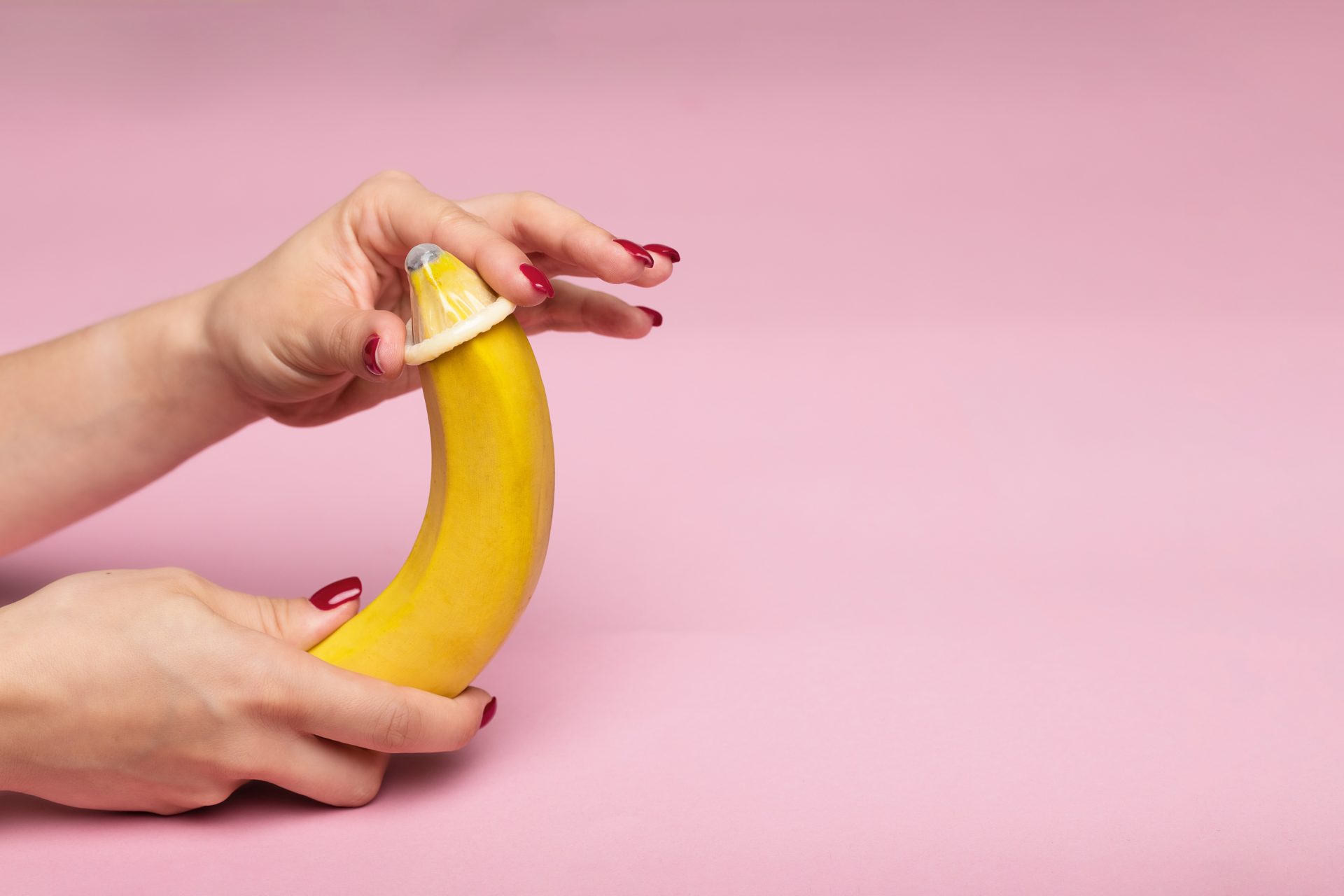 Close up shot of a person's hands putting a condom on a banana