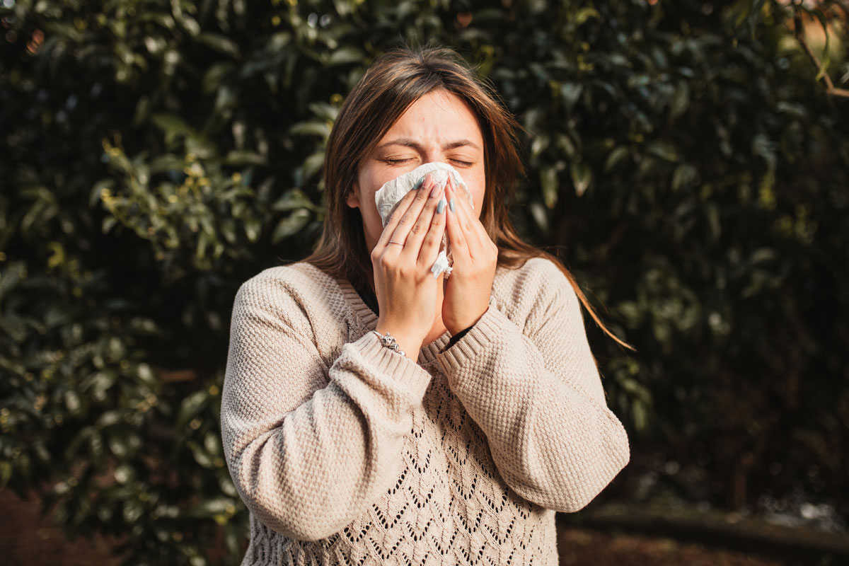 Young woman suffering spring allergy and blowing nose with a tissue in the nature - stock photo