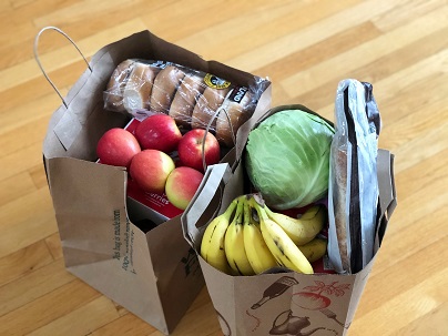 Two paper grocery bags full of groceries, including produce and bagels.