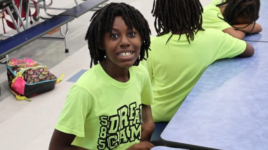 A young girl at a cafeteria table smiling for the camera