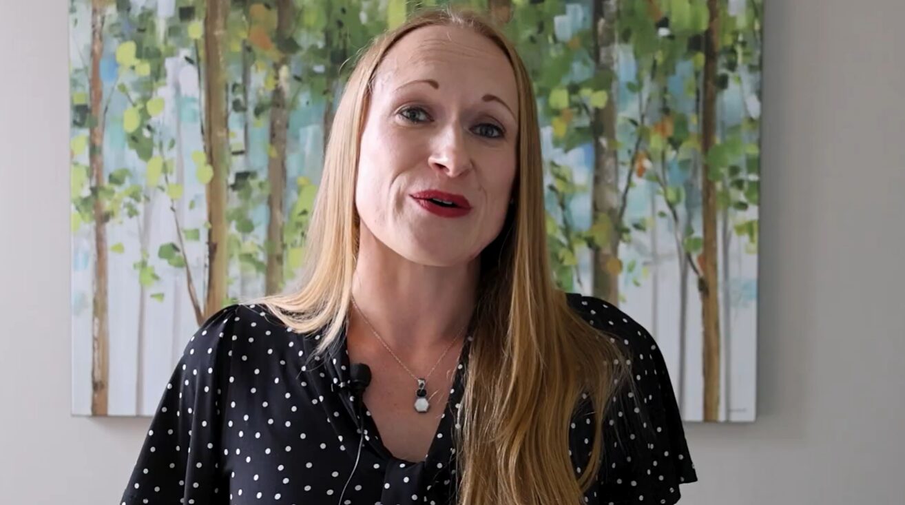 A woman talking to the camera in front of a painting