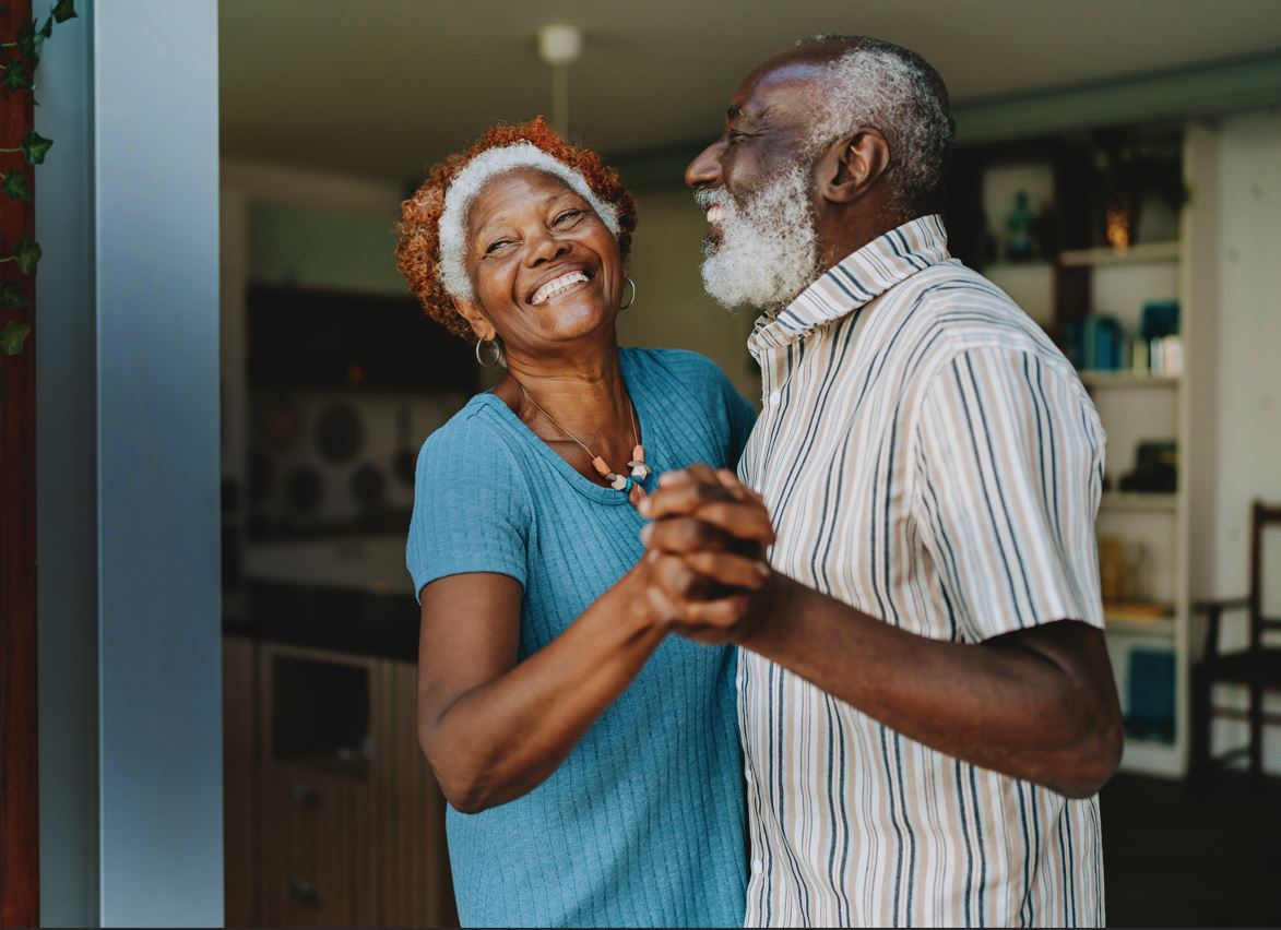 An older couple holding hands and dancing casually in their home
