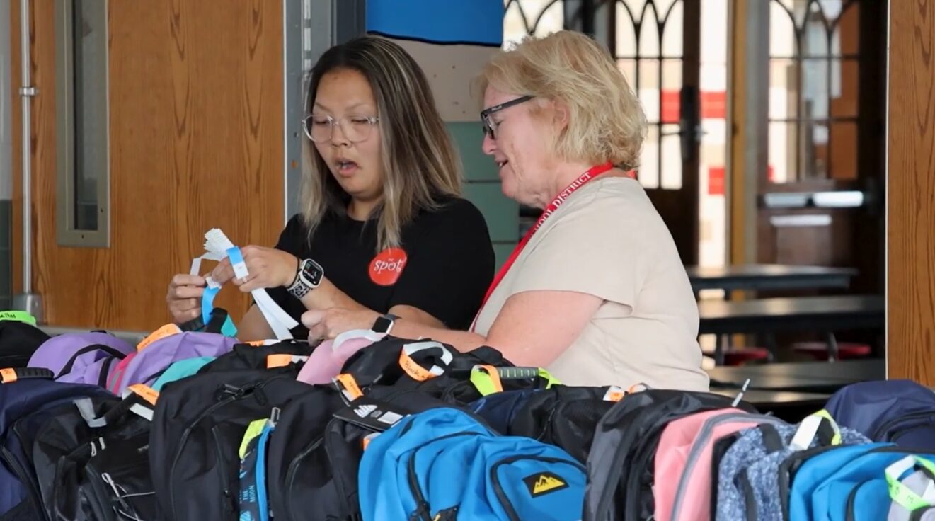Two women looking at a collection of donated backpacks
