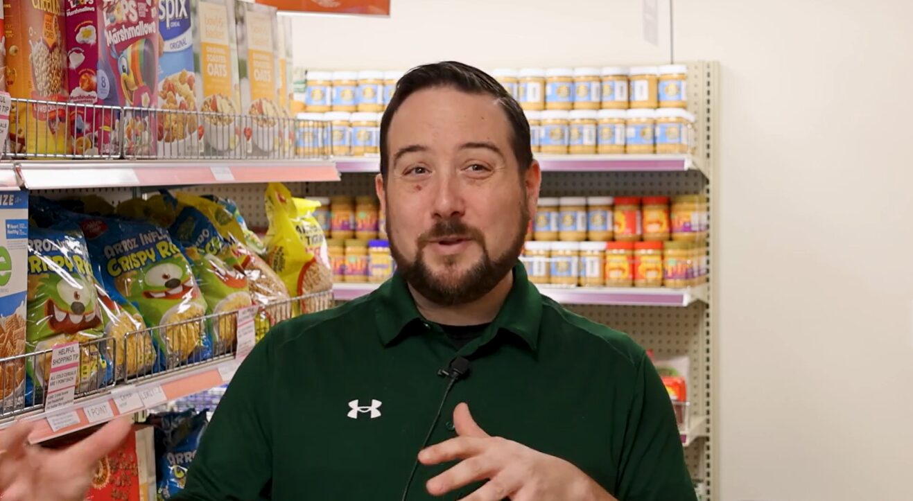 A volunteer talking to the camera in front of a grocery display