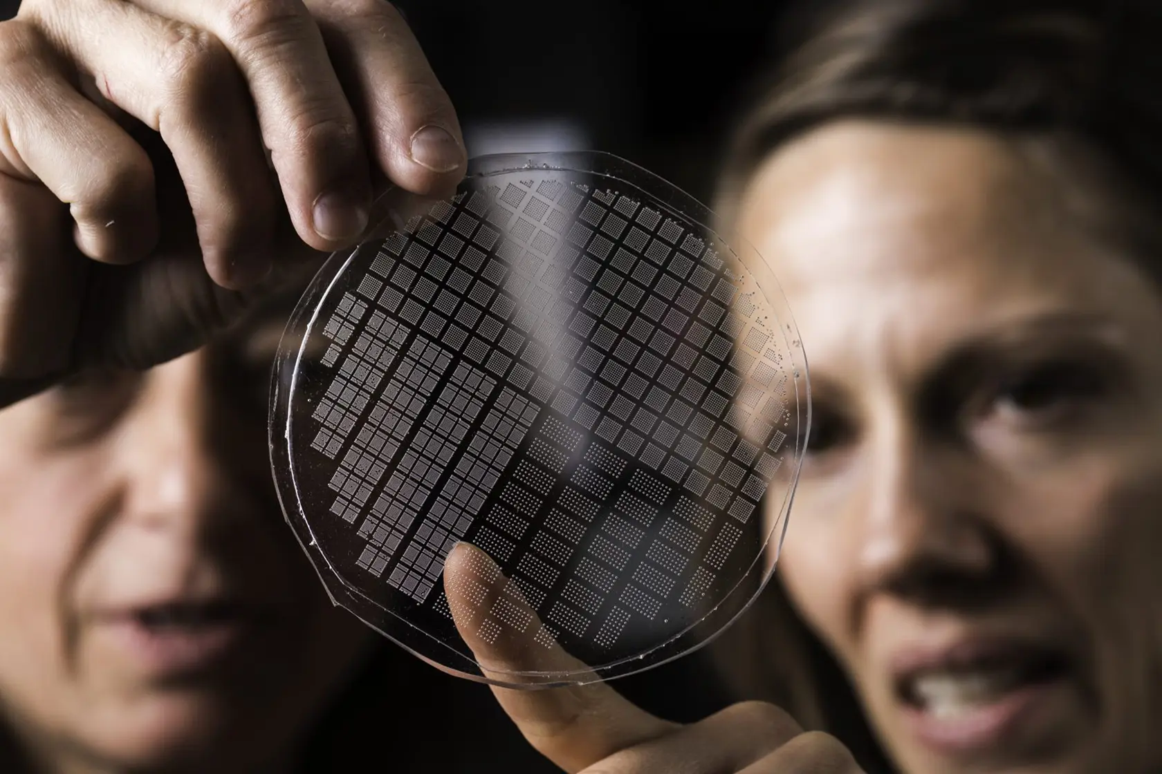 Two women proudly display a circular film plate featuring a distinctive grid pattern, showcasing their craftsmanship and creativity.