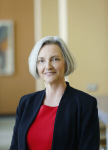 Martha Mock standing and smiling with black jacket and red shirt 
