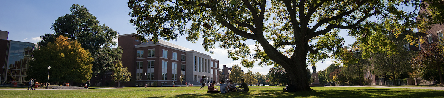 University of Rochester campus' Wilson quad with a view of the Warner School of Education building and students sitting on the grass.