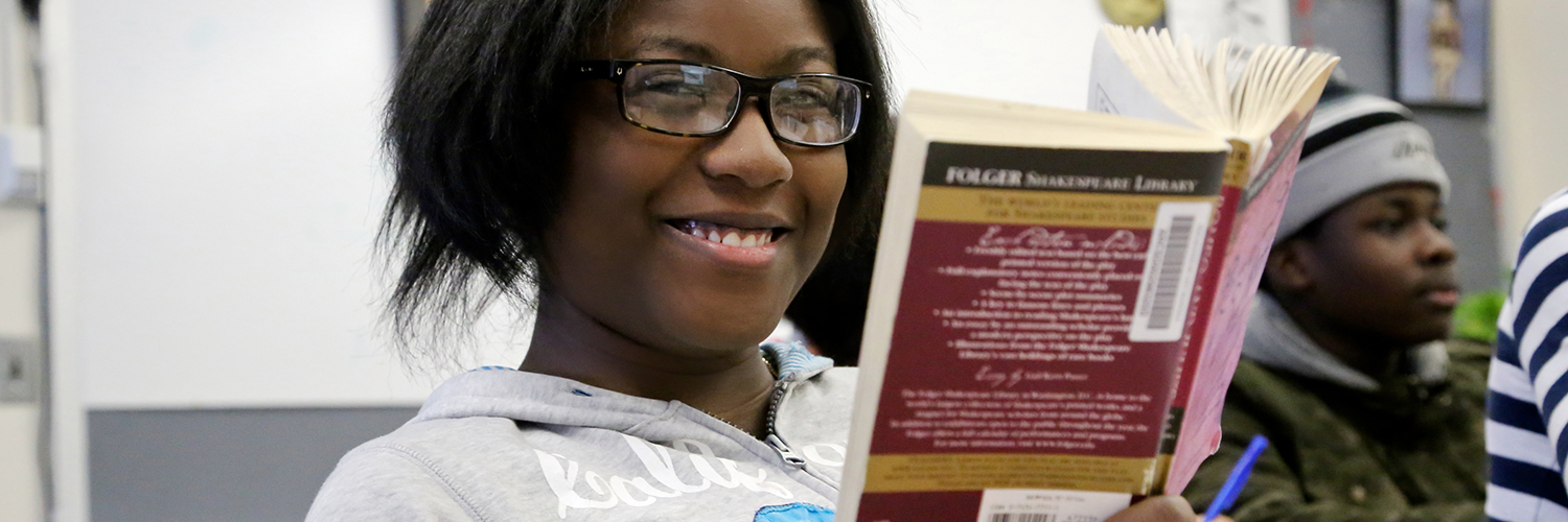 Smiling female student looking up from reading Romeo and Juliet